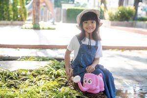 Asian little child girl pouring water on the trees. kid helps to care for the plants with a watering can in the garden. photo