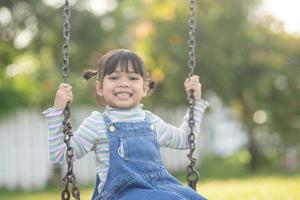 Happy little Asian girl playing swing outdoor in the park photo