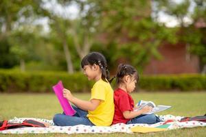 Little Girl and sister reading a book together in the park. Adorable Asian kids enjoying studying outdoors togther. Education, intelligence concept photo