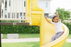 Child playing on outdoor playground. Kids play on school or kindergarten yard. Active kid on colorful slide and swing. Healthy summer activity for children. photo