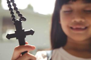 niña asiática rezando sosteniendo la cruz, concepto cristiano. foto