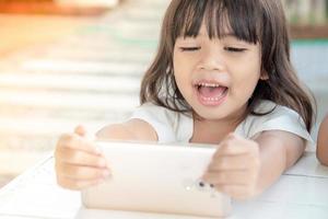 Little Asian girl using smart phone at cafe. Natural light outdoor lifestyle. photo