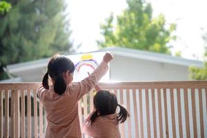 hermanos niña dibujando arco iris mira a través de la ventana durante la cuarentena covid-19. quedarse en casa campaña de redes sociales para el virus de la corona foto