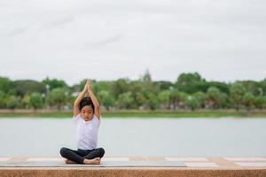 pequeña y linda niña asiática practicando pose de yoga en una alfombra en el parque, concepto saludable y de ejercicio foto