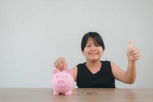 Cute asian child girl putting money into piggy bank to save money for the future photo