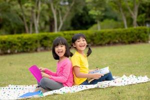 dos hermosas niñas leyendo libros en el jardín, sentadas en el césped. el concepto de educación y amistad. foto