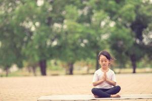 Little cute asian girl practicing yoga pose on a mat in park, Healthy and exercise concept photo