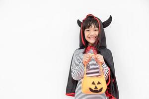 divertido concepto de niño de halloween, niña linda con disfraz de fantasma de halloween aterrador que sostiene un fantasma de calabaza naranja en la mano, sobre fondo blanco foto