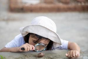 Happy kid girl exploring nature with a magnifying glass and a snail. He having fun in the garden. The concept of the kid is ready to go to school. photo