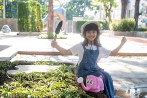 Asian little child girl pouring water on the trees. kid helps to care for the plants with a watering can in the garden. photo