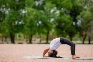 pequeña y linda niña asiática practicando pose de yoga en una alfombra en el parque, concepto saludable y de ejercicio foto