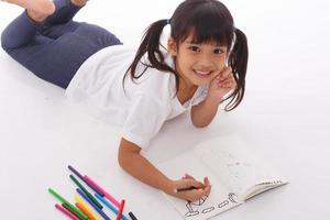 Cute little girl doing homework, reading a book, coloring pages, writing and painting. Children paint. Kids draw. Preschooler with books at home. photo