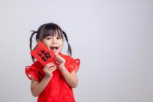 niña asiática feliz con vestido tradicional chino sonriendo y sosteniendo un sobre rojo. feliz concepto de año nuevo chino. foto