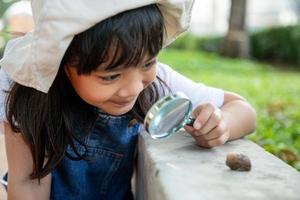 Happy kid girl exploring nature with a magnifying glass and a snail. He having fun in the garden. The concept of the kid is ready to go to school. photo
