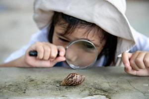 Happy kid girl exploring nature with a magnifying glass and a snail. He having fun in the garden. The concept of the kid is ready to go to school. photo