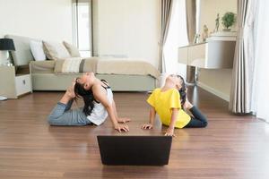 dos niñas practicando yoga, estiramientos, fitness por video en el cuaderno. entrenamiento de educación en línea distante, aeróbico en casa. estilo de vida saludable, coronavirus, quédate en casa. los niños hacen deporte en casa en cuarentena. foto