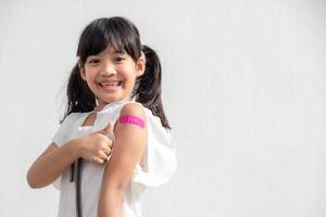 Asian little girl showing his arm after got vaccinated or inoculation, child immunization, covid delta vaccine concept photo