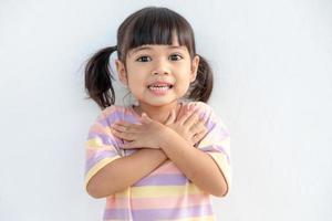 Close up of cute happy small girl isolated on white background hold hands at heart chest feel grateful, smiling little child with eyes closed pray thanking god high powers, faith concept photo