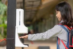 Child girls kid using automatic alcohol gel dispenser spraying on hands sanitizer machine antiseptic disinfectant, new normal life after Coronavirus COVID-19 pandemia. photo