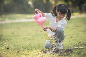 niña asiática vertiendo agua en los árboles. niño ayuda a cuidar las plantas con una regadera en el jardín. foto