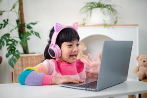 Smiling little Asian girl have a video call distant class with teacher using laptop, social distance during quarantine isolation during the Coronavirus photo