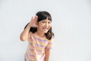 Little Asian girl holds her hand near her ear and listenings. Disability day.Deaf kid. Exciting face on Asian child girl. Turning off the phone and listening to your child.