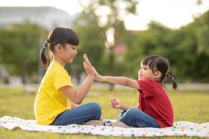 Two little girls sitting on the grass in the park and playing rock paper scissors hand game photo