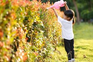 niña asiática vertiendo agua en los árboles. niño ayuda a cuidar las plantas con una regadera en el jardín. foto