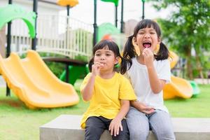 dos niños juegan y comen piruletas en el patio de recreo foto