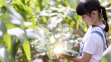 The little girl uses a tablet to analyze the growth of plants in the agricultural plot and visual icon., the agricultural technology concept. smart farming learning Concept photo