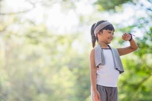 A little girl looks at smart watch after training in park. Healthy concept. Female after workout session checks results on watch.Children's sport concept photo
