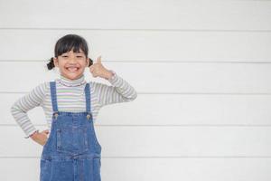 Portrait of little cute Asian girl with her thump up, advertisement concept, little Asian teenage thumps up with the white background and space photo