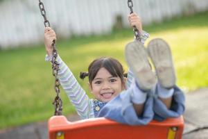 niña asiática feliz jugando al columpio al aire libre en el parque foto