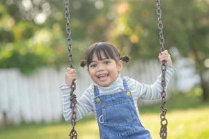 Happy little Asian girl playing swing outdoor in the park photo