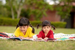 Little Girl and sister reading a book together in the park. Adorable Asian kids enjoying studying outdoors togther. Education, intelligence concept photo