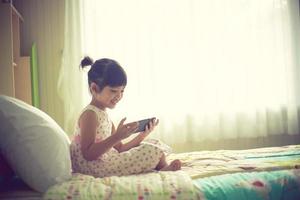 concepto de niño, tecnología e internet - niña acostada en la cama con smartphone en casa foto