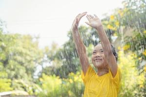 Happy Asian little child girl having fun to play with the rain in the sunlight photo