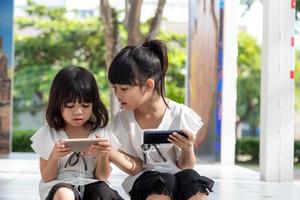 Concept kids and gadgets. Two little girls siblings sisters look at the phone and smile. They hold a smartphone watch videos, learn, play games, speak online. Internet for children. Parental control photo