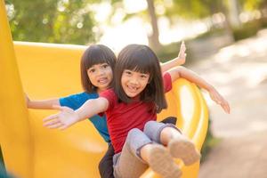 Cute little girls siblings having fun on playground outdoors on sunny summer day. Children on plastic slide. Fun activity for kid. active sport leisure for kids photo