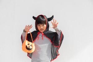 divertido concepto de niño de halloween, niña linda con disfraz de fantasma de halloween aterrador que sostiene un fantasma de calabaza naranja en la mano, sobre fondo blanco foto