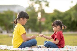 dos niñas sentadas en el césped del parque y jugando al juego de manos de piedra, papel y tijera foto