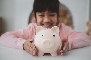 niña asiática ahorrando dinero en una alcancía, aprendiendo a ahorrar, los niños ahorran dinero para la educación futura. concepto de dinero, finanzas, seguros y personas foto