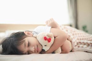 child little girl sleeps in the bed with a toy teddy bear photo