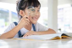 niña asiática leyendo los libros en el escritorio con una lupa foto