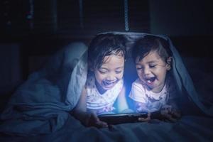 Cute girl looking at his younger sister who is playing a game on a smart phone on bed photo