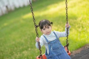 Happy little Asian girl playing swing outdoor in the park photo