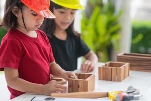 hermanos asiáticos niñas con sombreros de ingeniería construyendo casa con el juguete de madera. para aprender y mejorar el desarrollo, pequeño arquitecto. foto