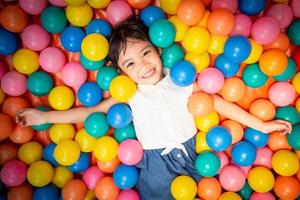 niña asiática feliz jugando en la piscina de bolas de colores foto
