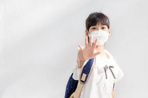 Back to school.Little Asian girl wearing a mask for protection. show stop hands gesture to stop coronavirus outbreak. photo