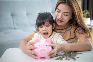 madre e hija poniendo monedas en la alcancía. presupuesto familiar y concepto de ahorro. concepto de cuenta de ahorro junior foto